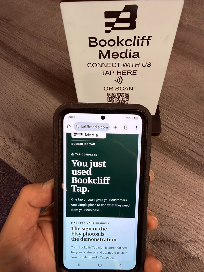 Phone displaying a Bookcliff Tap Page in front of a personalized acrylic Tap Sign on its stand